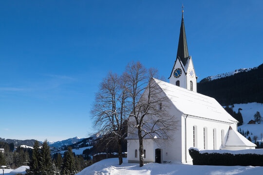 Picturesque little church covered with snow in a winter landscape in Hirschegg in Kleinwalsertal in Allgäuer Alpen, Vorarlberg in Austria. Blue sky