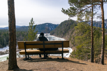 Back view of a young guy sitting on a bench over the river canyon