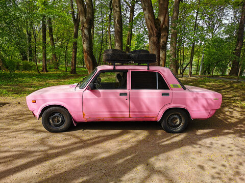 An old Soviet pink car stands among the trees in a park on Elagin Island in St. Petersburg.