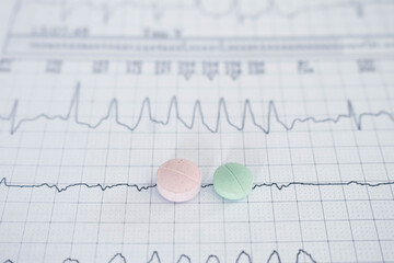 Pills or medications on sheets of paper with EKGs. Cardiac arrhythmias represented on paper.