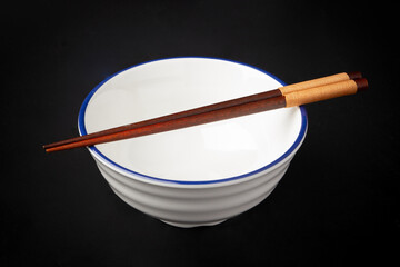 White bowl is empty, and chopsticks are placed on top of the bowl isolated on a black background.