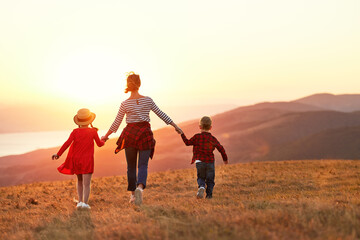 Happy family: mother with children son and daughter running on nature on sunset