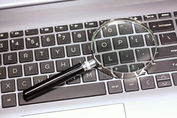 Magnifying glass laying on a modern laptop keyboard, loupe on top of a netbook, file search, pc forensic investigation. Web information search, data search engine simple concept, closer look, nobody