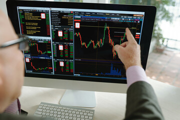 Over shoulder view of stock market analyst pointing at computer monitor while working with colorful graph