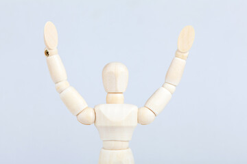 Wooden figurine, doll, man surrendering or celebrating, throwing hands up in the air, object closeup. Gestures, body language. Person capitulating, giving in or raising arms excited concept, nobody