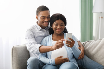 Loving black expecting parents shopping online, using smartphone