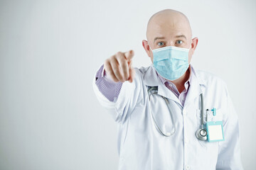 Portrait of mature bald Caucasian doctor with badge standing against white background and pointing with finger at you