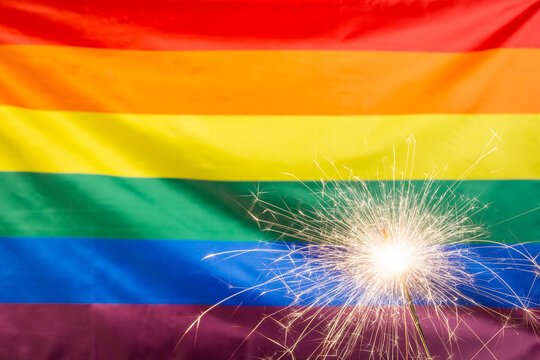 Glowing sparkler against waving LGBT flag with copy space