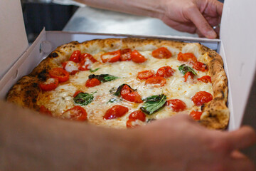 Pizza napoletana con pomodorini freschi, mozzarella di bufala e basilico mentre viene chiusa in un cartone d'asporto per le pizze