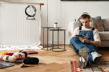 Young man in headphones using tablet computer while working on craft rug