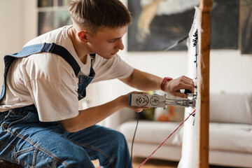 Young white man working on craft rug with sewing machine