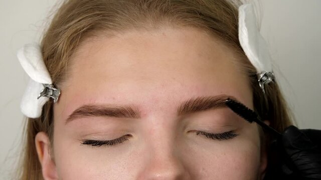 Stylist's hands combing patient’s eyebrows with a special brush before plucking. Gloved master shaping eyebrow with a cosmetic brush close-up. Beautiful attractive female face 
