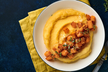 Polenta with butter, pumpkin, garlic, savory and parmesan cheese in white bowl on dark blue concrete background. Traditional Basic Italian food, vegan food. Top view. Copy space.