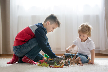 Blond child, toddler boy and his older brother, preteeen boy, playing with plastic animal toys at...