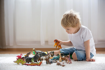 Blond child, toddler boy, playing with plastic animal toys at home