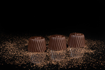 Chocolate candies on a dark background with reflection. Piece by piece and as a whole. Filling of nuts and fruits.