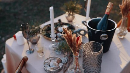The close frame of a decor. Romantic dinner in nature, table with flowers, candles, cutlery and champagne. The beauty of nature in the evening