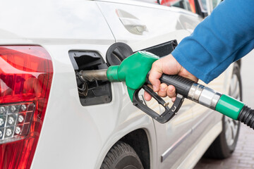 Man's hand holds green gas pump in car tank during process of refueling car with gasoline or...
