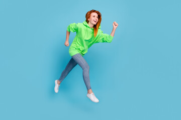 Fototapeta na wymiar Photo of charming cute young woman wear green sweatshirt jumping running empty space smiling isolated blue color background