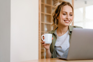Young white woman smiling while drinking coffee and using laptop