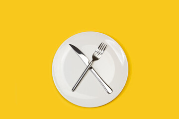 Cubiertos, cuchillo y tenedor cruzados arriba de un plato redondo blanco sobre un fondo amarillo...