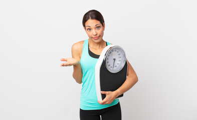 young hispanic woman feeling puzzled and confused and doubting and holding a scale