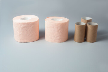 Two rolls of pink toilet paper and a few sleeves from them stand on a gray background.