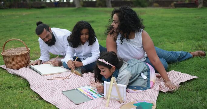 Happy indian parents having fun at city park painting with their children - Family, summer and love concept 