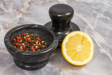 Lemon and stone bowl with peppercorn on gray background.