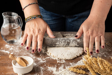 Top view of woman's hands kneading with rolling pin, on wooden table with flour, jug of water, salt and wheat, horizontal