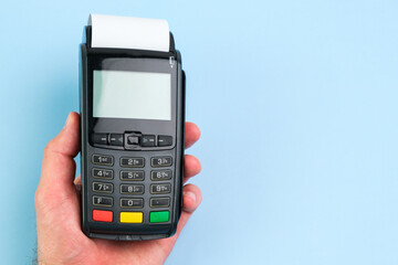 Man hand pushing a button on POS terminal with roll paper cash tape on the blue background