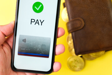 Application for payment on the smartphone screen on the wallet with bitcoins on the yellow background.