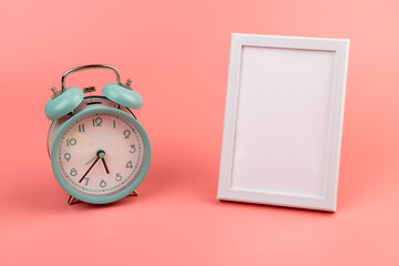 Photo frame and blue alarm clock on pink background with copy space.