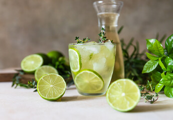 Cold refreshing summer drink or lemonade with lime and thyme on concrete background.