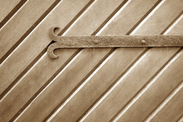 Old metal door hinge on wooden door in brown tone.