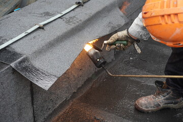 Flat roof installation with propane blowtorch during construction works with roofing felt. Heating and melting bitumen roofing felt.