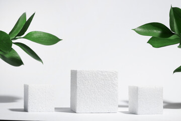 White porous cube, square podium with leaves and shadows on a white gray background. Conceptual scene, showcase for a new product, presentation, sale, advertisement, banner, cosmetics. With copy space