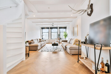 Perspective view of light colored room with sofas and rug on parquet floor and spiral white staircase leading to second floor