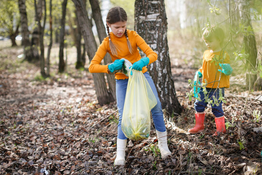 children clean up in the park. Two children collect garbage in the forest. Children in yellow turtlenecks and jeans in the spring forest