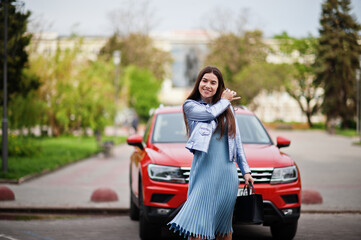 Outdoor photo of gorgeous woman with handbag posing near orange suv car.