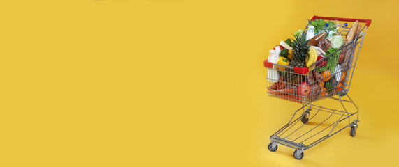 Shopping cart full of groceries on yellow background. Space for text