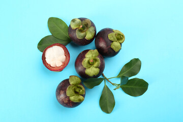 Fresh ripe mangosteen fruits with green leaves on turquoise background, flat lay