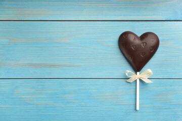 Chocolate heart shaped lollipop on turquoise wooden table, top view. Space for text