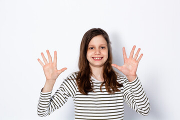 A funny dark-haired girl shows her 10 fingers with her hands forward. On a light background. Place for your text.