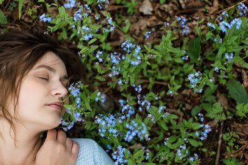 Girl in meadow of forget-me-nots has a lot of space on side. Eyes are closed.
