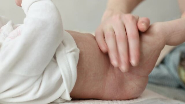 Mother hands stroking legs and body of infant with love. Close-up baby foot massage. Air Bath after diapers