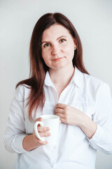 Portrait of a beautiful woman in a white shirt with a ceramic mug in her hands on a white background. Woman drinking water coffee tea from white mug cup