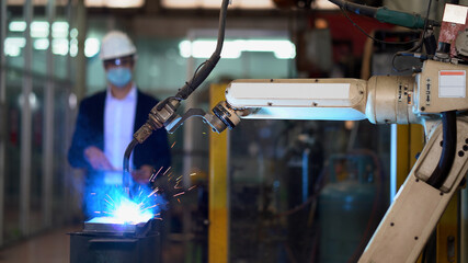 Manager engineer using digital tablet control  Welding robot arms machine in factory industry.  business man wearing face mask checking monitoring system software of robotics automatic . technology