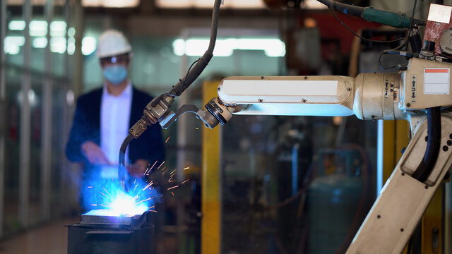 Manager engineer using digital tablet control  Welding robot arms machine in factory industry.  business man wearing face mask checking monitoring system software of robotics automatic . technology - Powered by Adobe