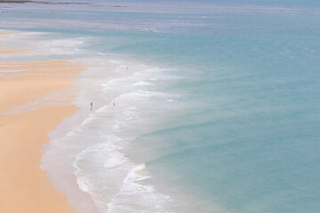 Top view on a sand beach with incoming tide and very few people at the coastline of Normandy